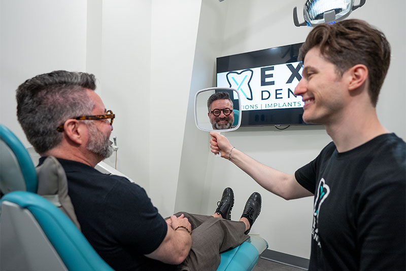 doctor holding up mirror so patient can see their smile after dental implants
